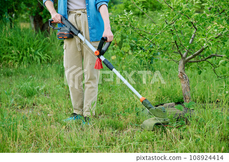 Woman mowing grass with cordless trimmer in garden 108924414