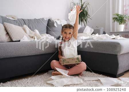 The process of creating a mess by a child. Little girl scatters napkins in living room 108925248