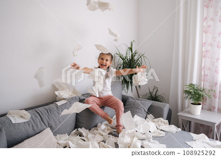 Adorable little girl make a mess at home. Five year old girl throws napkins in living room 108925292