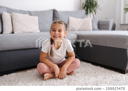 Active and energetic little girl have fun and home. Living room. Kid sitting on the carpet. 108925478