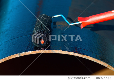 Metal pipe is painted with paint roller with black paint or bitumen. Protection of metal pipes from 108925648