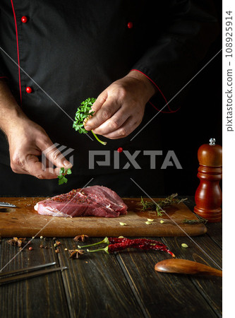 Adding parsley to steak for aroma and taste. Cooking veal shish kebab on the kitchen table by the hands of a chef Adding parsley to steak for aroma and taste. Cooking veal shish kebab on the kitchen table by the hands of a chef 108925914