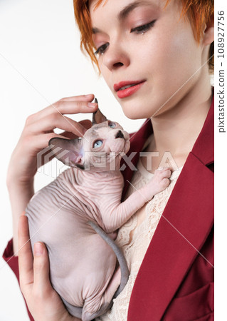Hipster young redhead woman with short hair gently hugging to her chest Canadian Sphynx Cat 108927756