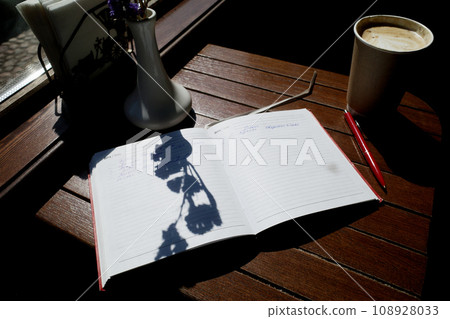 Breakfast in a coffee shop with a diary. A cup of coffee, a shadow on paper. Writing practices Breakfast in a coffee shop with a diary. A cup of coffee, a shadow on paper. Writing practices 108928033