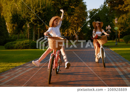 Happy funny young girl with female friend riding on bicycle with raised legs 108928889