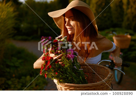 Charming lady smelling wildflower blossoms during bicycle walk in park 108928890