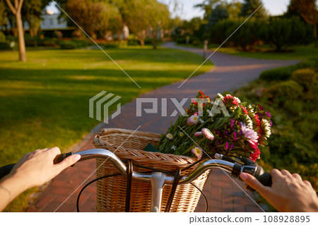 Closeup woman riding bicycle with flower basket handlebar view 108928895
