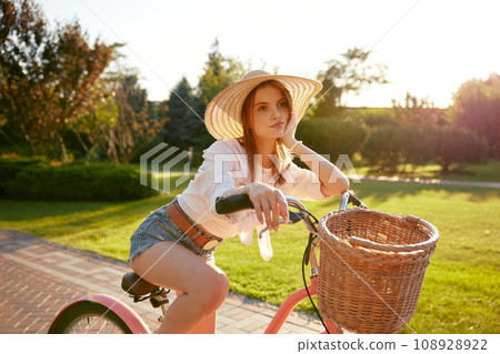 Dreamy romantic teenager girl riding bicycle in summer park 108928922