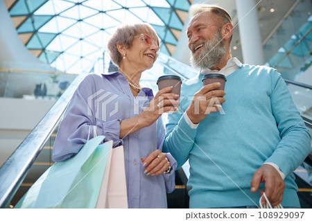 Senior couple riding down shopping mall escalator 108929097