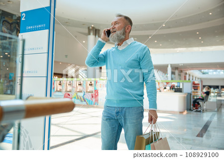 Stylish senior man with phone walking with purchases 108929100