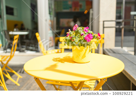 Outdoor cafe with yellow furniture on the seashore.The cafe is decorated with planters with plants installed between the tables.  108929221