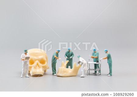 Miniature people Doctor with a giant human skull on a grey background 108929260