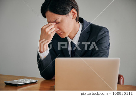 Young male office worker putting his hand between his eyebrows Young male office worker putting his hand between his eyebrows 108930111