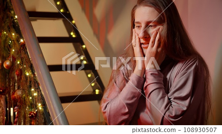 Young woman got scared and nervous on Christmas night. Police or ambulance car lights illuminating the room. Crime, ambulance, injury, problems with law and theft on winter holidays and celebrations. 108930507