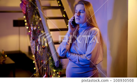Portrait of nervous woman talking to emergency service on Christmas night. Police car lights illuminate the room. Crime, ambulance, injury, problems with law and theft on winter holidays and Portrait of nervous woman talking to emergency service on Christmas night. Police car lights illuminate the room. Crime, ambulance, injury, problems with law and theft on winter holidays and 108930508