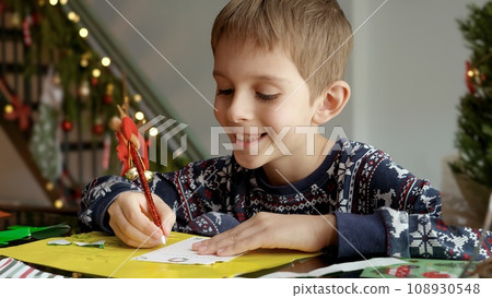 Portrait of little boy in pajamas writing a letter to Santa Claus with his wishes. 108930548