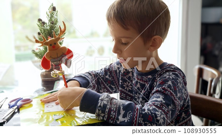 Portrait of thoughtful little boy thinking of what to wish on Christmas while writing letter to Santa 108930555