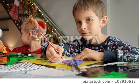 Portrait of little boy with brother sitting on kitchen and writing letter to Santa on Christmas. 108930612