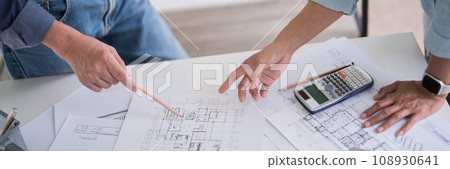 Two engineer architect pointing on blueprint of sketching interior architectural building to discussion technical for construction plan and building model while working together in workplace site 108930641