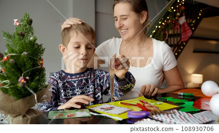 Happy boy with mother making handmade Christmas postcards and greeting cards while preparing for winter holidays. Winter holidays, family time together, kids with parents celebrating. 108930706