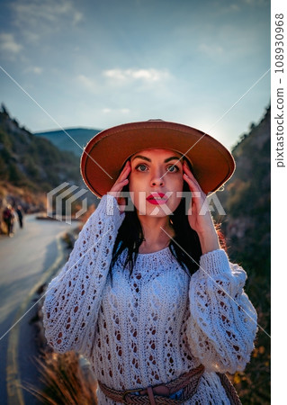Woman road mountain. A woman in a white sweater, black boots and a hat walks along a winding alpine path between the mountains at sunset in late summer. The concept of travel. Woman road mountain. A woman in a white sweater, black boots and a hat walks along a winding alpine path between the mountains at sunset in late summer. The concept of travel. 108930968