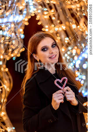 Christmas mood. Woman with long hair in sity decorated for Christmas. She is dressed in a black coat. 108931068