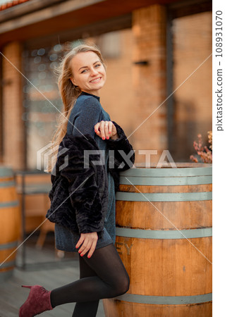 Christmas mood. Young blonde with long hair near the cafe, decorated for Christmas. She is dressed in a black short fur coat and a blue short dress. 108931070