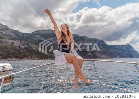 Woman on a yacht. Happy model in a swimsuit posing on a yacht against a blue sky with clouds and mountains 108931076