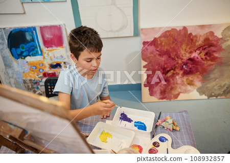 Top view Caucasian elementary age school student boy holding paintbrush and mixing watercolors on a palette at art class 108932857