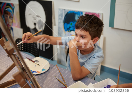 Teen boy expressing himself while drawing on canvas, holding paintbrush and oil painting pictures in creative workshop 108932866