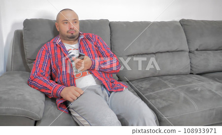 Bachelor man enjoy weekends resting lean sit on comfy sofa in living room alone, hold remote control switch channel watch tv relaxing at home spend lazy time. Streaming digital television ad concept Bachelor man enjoy weekends resting lean sit on comfy sofa in living room alone, hold remote control switch channel watch tv relaxing at home spend lazy time. Streaming digital television ad concept 108933971