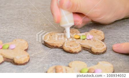 woman's hands decorating a gingerbread man-shaped Christmas cake with white icing and colored caramels, close-up 108934032