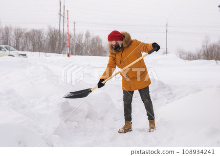 Man is clearing the snow near house and on staircases hovelling at the winter season. Winter storm and season specific Man is clearing the snow near house and on staircases hovelling at the winter season. Winter storm and season specific 108934241
