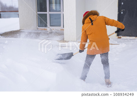 Man is clearing the snow near house and on staircases hovelling at the winter season. Winter storm and season specific 108934249