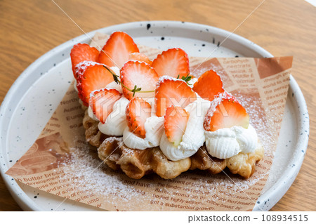 Yummy waffles with whipped cream, strawberries and caramel syrup on table, top view shot Yummy waffles with whipped cream, strawberries and caramel syrup on table, top view shot 108934515