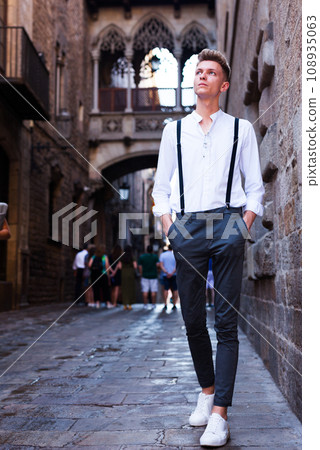 Young European guy in shirt and trousers with suspenders walking around city 108935063