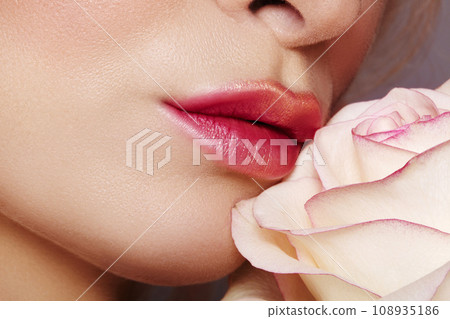 Close-up of beautiful lips with bright red kissed makeup and gold glitter. Fashion visage with white rose flower Close-up of beautiful lips with bright red kissed makeup and gold glitter. Fashion visage with white rose flower 108935186