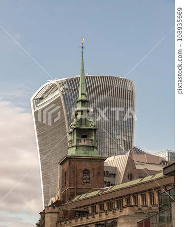 View of The copper green spire steeple of All Hallows by the Tower church (Ancient Anglican church) with The modern 20 Fenchurch Street (Walkie-Talkie building) skyscraper is behind. Contrasts of View of The copper green spire steeple of All Hallows by the Tower church (Ancient Anglican church) with The modern 20 Fenchurch Street (Walkie-Talkie building) skyscraper is behind. Contrasts of 108935669