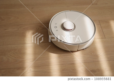 Round wireless autonomous robotic vacuum cleaner on wooden floor with sunlights. Household remote control appliances. Smart cleaning technology. Self-propelled cleaning robot. Floor cleaning system 108935681