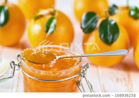 Close-up of glass jar with orange jam on white table with fresh fruits, selective focus. 108936258