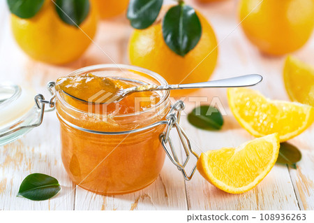 Spoon with delicious orange marmalade or jam over jar on table. Space for text. Spoon with delicious orange marmalade or jam over jar on table. Space for text. 108936263