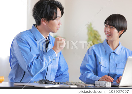 Three male and female engineers having a discussion about prototypes such as circuit boards while looking at a PC 108937007