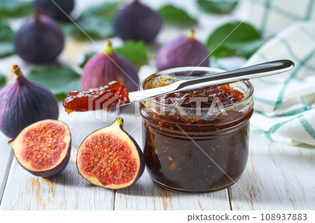 Sweet figs jam in jar with figs slices on wooden table. Delicious figs jam on table close-up. 108937883