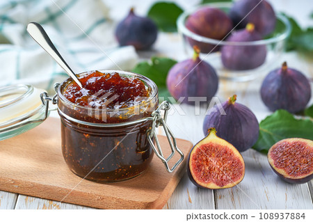 Homemade jam. A glass jar of figs jam on a white wooden table. Homemade figs marmalade and fresh figes and green leafs on the kitchen table. 108937884