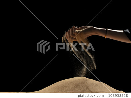 Hand releasing dropping sand on hill. Fine Sand flowing pouring through fingers hand against black background. Summer sand hill beach holiday vacation and time passing concept. Isolated freeze shot 108938228