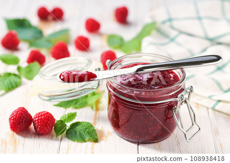 Sweet raspberry jam in jar with fresh berries on wooden table. Delicious raspberry jam on table close-up. Sweet raspberry jam in jar with fresh berries on wooden table. Delicious raspberry jam on table close-up. 108938418