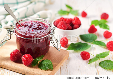 Homemade raspberry confiture in a jar on a white wooden table. Delicious homemade natural raspberry jam. Homemade raspberry confiture in a jar on a white wooden table. Delicious homemade natural raspberry jam. 108938419