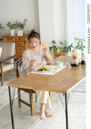 A woman eating while watching a smartphone 108939950