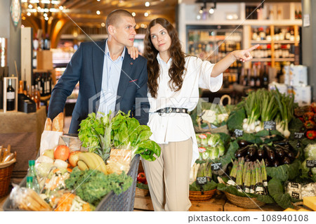 Beautiful woman points with her hand to her man at something in grocery store Beautiful woman points with her hand to her man at something in grocery store 108940108