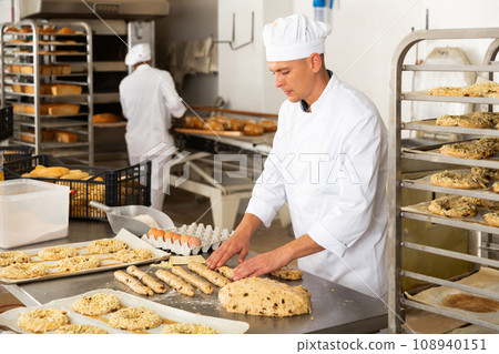 Baker makes buns and other sweet pastries from dough Baker makes buns and other sweet pastries from dough 108940151
